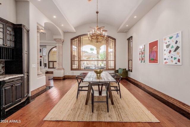 dining area with hardwood / wood-style floors, decorative columns, an inviting chandelier, and lofted ceiling