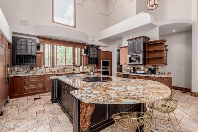 kitchen featuring decorative backsplash, light stone counters, a large island with sink, a high ceiling, and a breakfast bar area