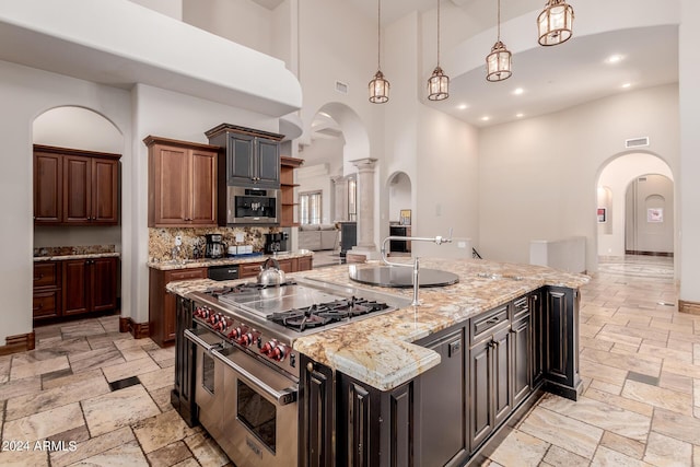 kitchen with pendant lighting, a large island with sink, a towering ceiling, dark brown cabinetry, and stainless steel appliances