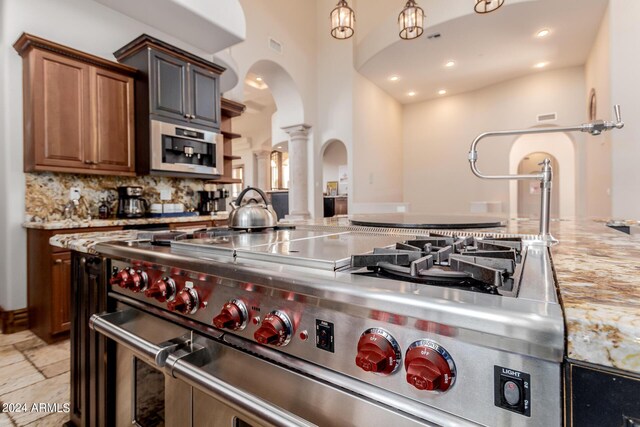 kitchen with ornate columns, light stone countertops, backsplash, a towering ceiling, and appliances with stainless steel finishes