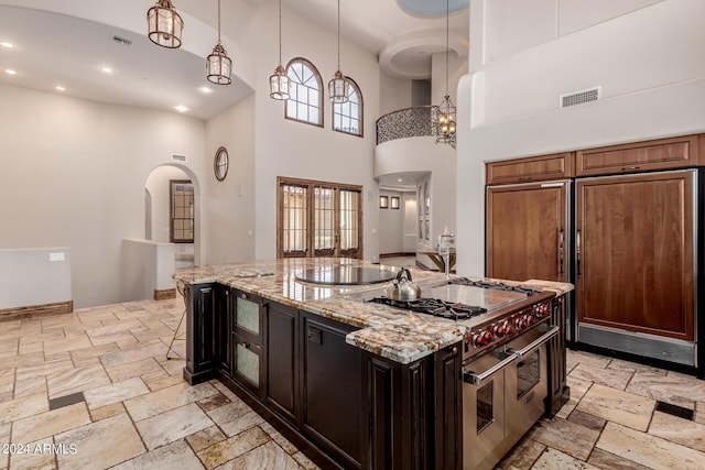 kitchen featuring light stone countertops, a high ceiling, pendant lighting, high quality appliances, and a center island with sink