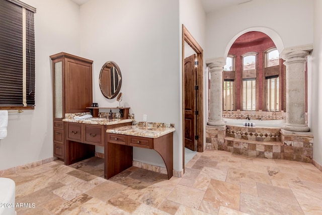 bathroom featuring vanity, decorative columns, and tiled tub