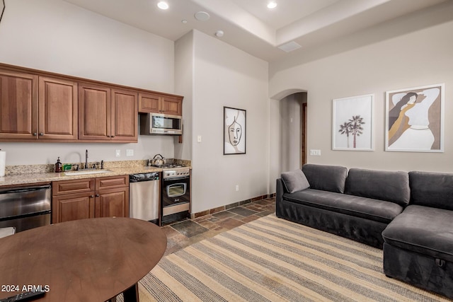 kitchen featuring light stone counters, sink, stainless steel appliances, and a high ceiling