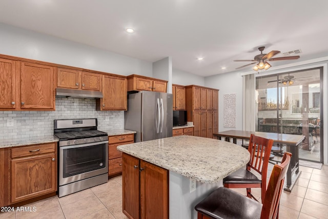 kitchen featuring backsplash, light stone countertops, a kitchen island, and appliances with stainless steel finishes