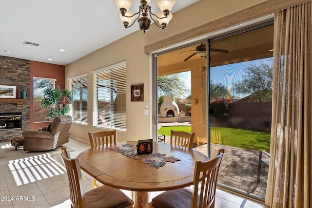 tiled dining room with ceiling fan with notable chandelier and a stone fireplace