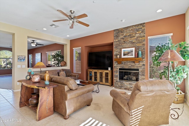 tiled living room featuring a stone fireplace and ceiling fan