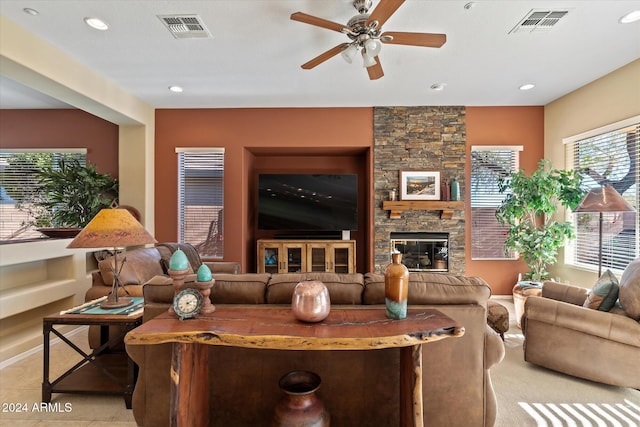 tiled living room with ceiling fan and a stone fireplace