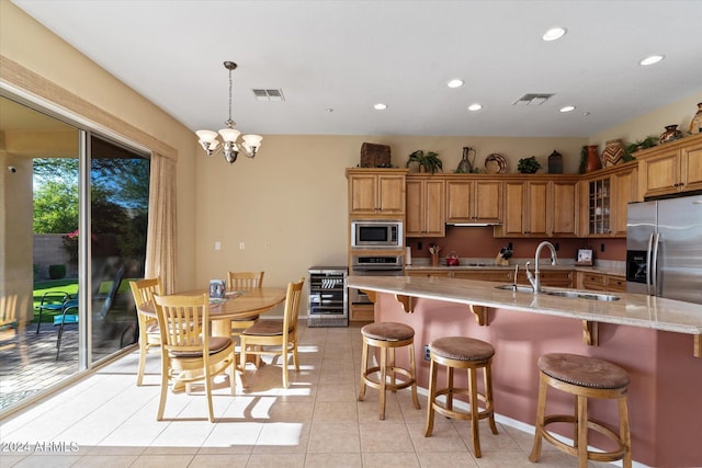 kitchen featuring pendant lighting, a large island with sink, light stone countertops, appliances with stainless steel finishes, and a notable chandelier