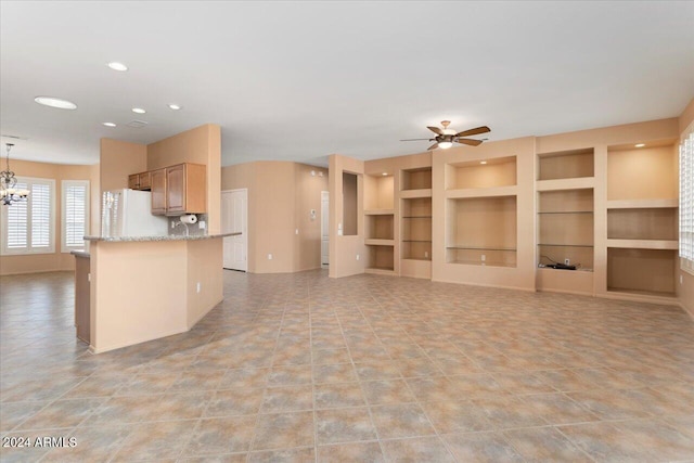 kitchen featuring light stone counters, freestanding refrigerator, ceiling fan with notable chandelier, built in shelves, and recessed lighting