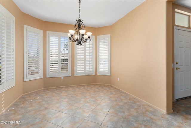 unfurnished dining area with tile patterned flooring, a notable chandelier, and baseboards