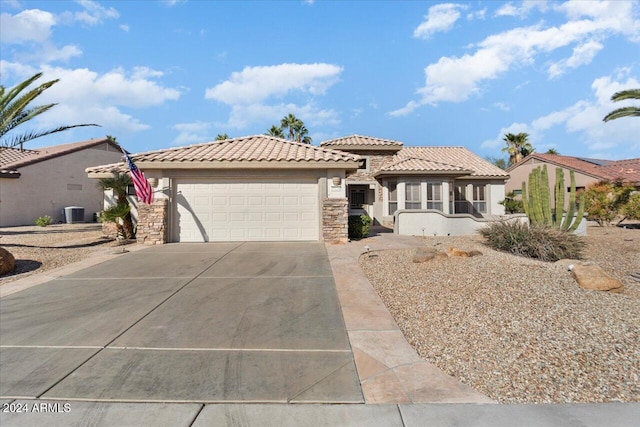 mediterranean / spanish-style home with driveway, stone siding, a tile roof, an attached garage, and stucco siding