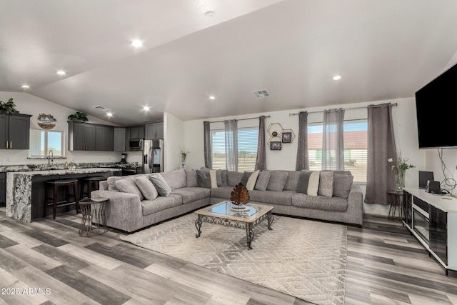 living room with lofted ceiling, light hardwood / wood-style floors, and sink