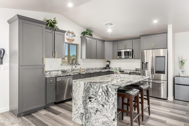 kitchen with stainless steel appliances, gray cabinetry, light stone counters, and a center island