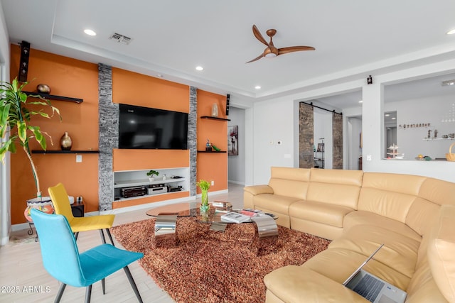 living room with built in shelves, a barn door, and ceiling fan