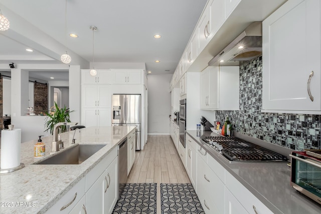 kitchen with sink, white cabinets, a barn door, stainless steel appliances, and light stone countertops