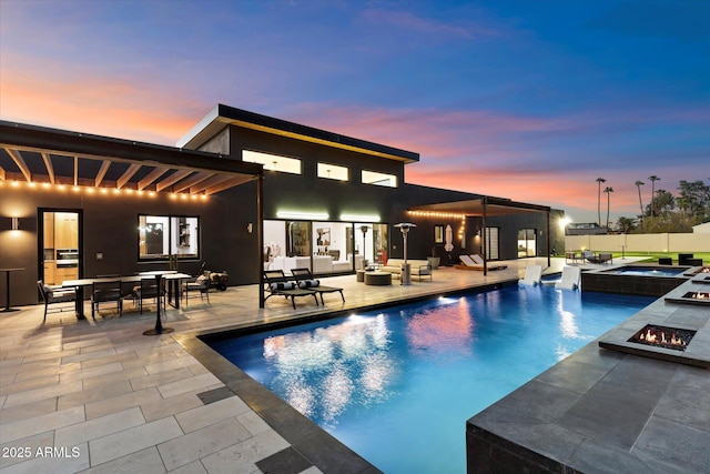 view of pool with a pool with connected hot tub, an outdoor living space with a fire pit, fence, outdoor dining area, and a patio area