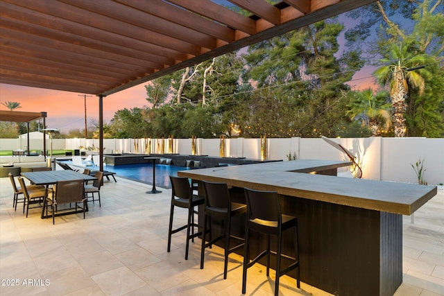 patio terrace at dusk with a fenced in pool, a fenced backyard, and outdoor dry bar