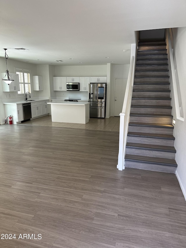 kitchen with appliances with stainless steel finishes, sink, white cabinets, a center island, and hanging light fixtures