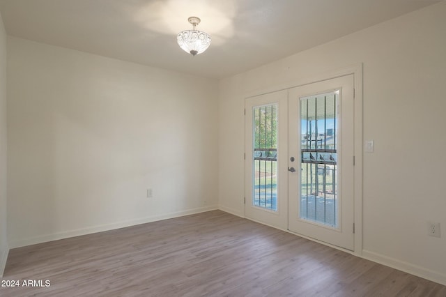 unfurnished room featuring a chandelier, light wood-type flooring, and french doors