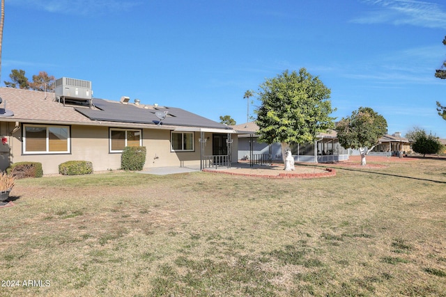 rear view of house with a sunroom, solar panels, a lawn, cooling unit, and a patio