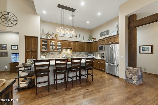 kitchen with a kitchen bar, light hardwood / wood-style flooring, pendant lighting, stainless steel appliances, and decorative backsplash