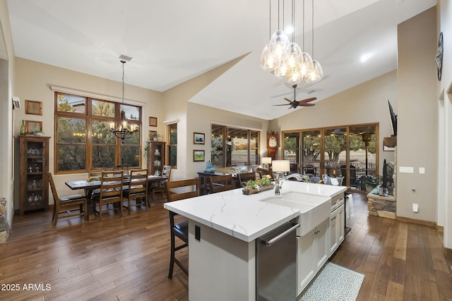 kitchen featuring light stone counters, decorative light fixtures, stainless steel dishwasher, and an island with sink