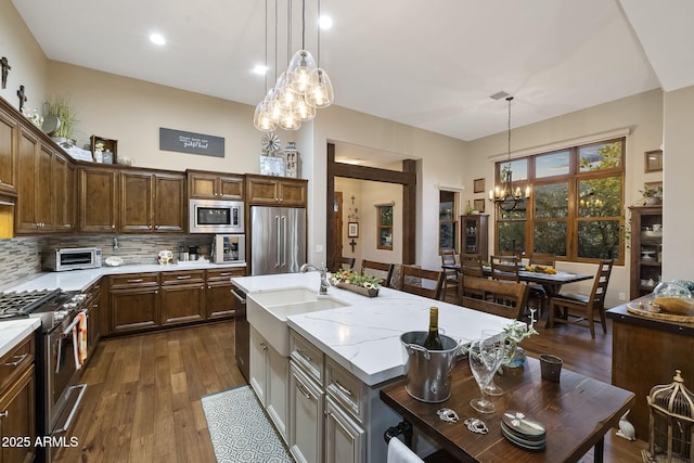 kitchen with tasteful backsplash, a center island with sink, appliances with stainless steel finishes, pendant lighting, and light stone countertops