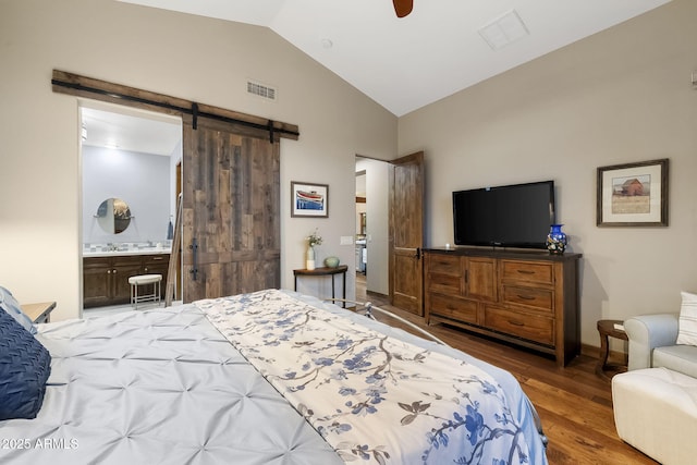 bedroom featuring dark wood-type flooring, ceiling fan, connected bathroom, vaulted ceiling, and a barn door