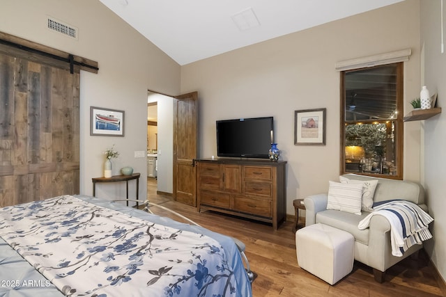 bedroom featuring hardwood / wood-style flooring, lofted ceiling, and a barn door