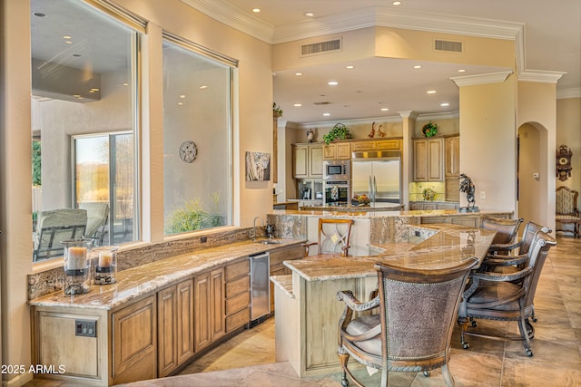 kitchen featuring kitchen peninsula, a kitchen bar, built in appliances, and light stone counters