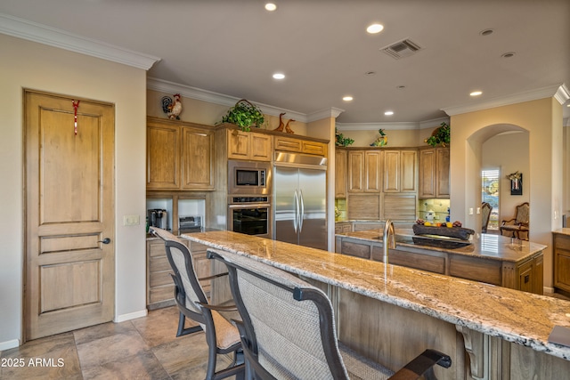 kitchen with a breakfast bar area, built in appliances, light stone counters, and ornamental molding