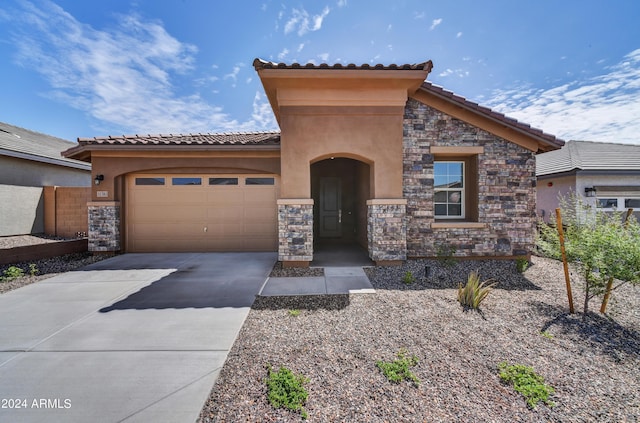 mediterranean / spanish home with stone siding, driveway, an attached garage, and stucco siding