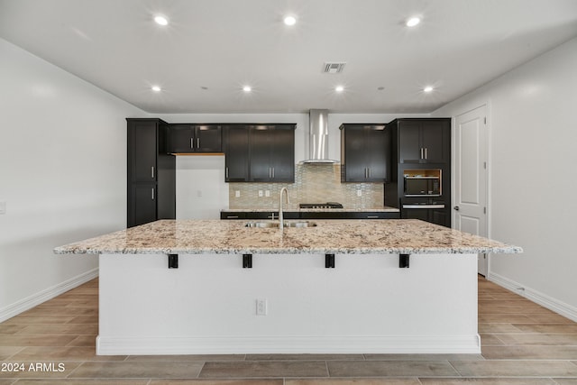 kitchen featuring wall chimney range hood, a sink, a large island, and wood tiled floor