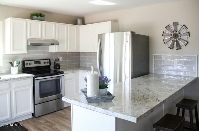 kitchen with under cabinet range hood, white cabinetry, appliances with stainless steel finishes, backsplash, and light wood finished floors