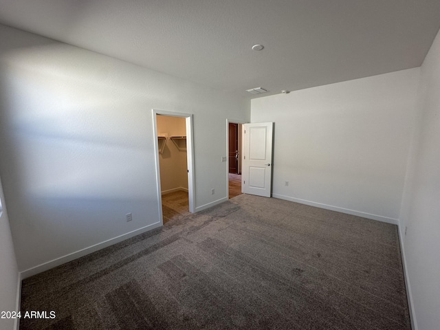 unfurnished bedroom featuring dark colored carpet, a spacious closet, and a closet