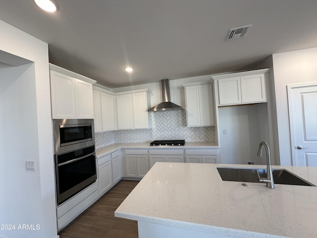 kitchen featuring light stone countertops, sink, wall chimney exhaust hood, dark wood-type flooring, and stainless steel appliances