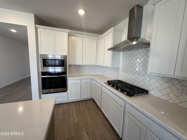 kitchen featuring white cabinetry, light stone countertops, wall chimney exhaust hood, dark hardwood / wood-style flooring, and appliances with stainless steel finishes