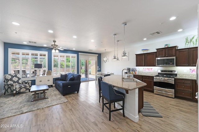 kitchen featuring sink, stainless steel appliances, light stone counters, light hardwood / wood-style flooring, and a breakfast bar