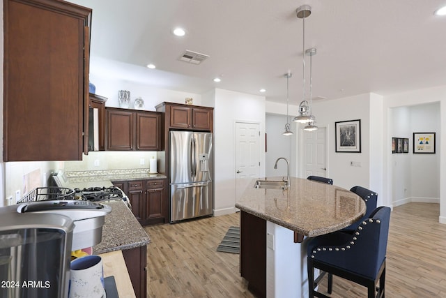 kitchen featuring stainless steel fridge, a center island with sink, hanging light fixtures, and sink