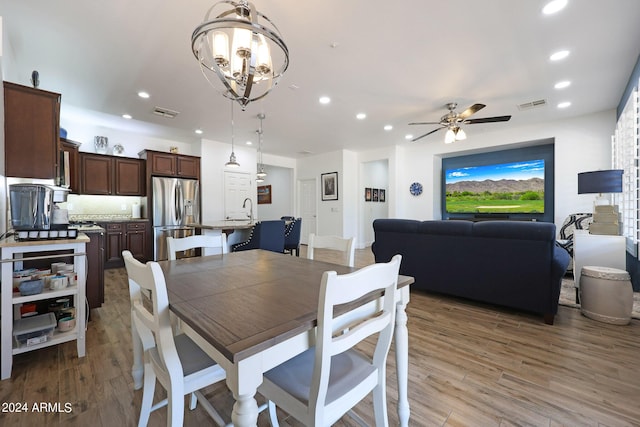 dining area featuring ceiling fan with notable chandelier, hardwood / wood-style flooring, and sink