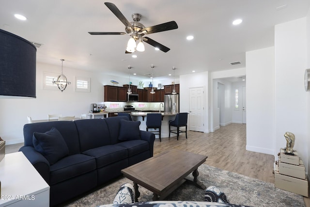 living room with light hardwood / wood-style flooring, ceiling fan with notable chandelier, and sink