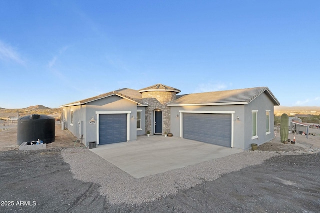 view of front of property featuring an attached garage, concrete driveway, stone siding, a tiled roof, and stucco siding