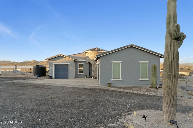 view of front facade featuring concrete driveway, stone siding, an attached garage, a mountain view, and stucco siding