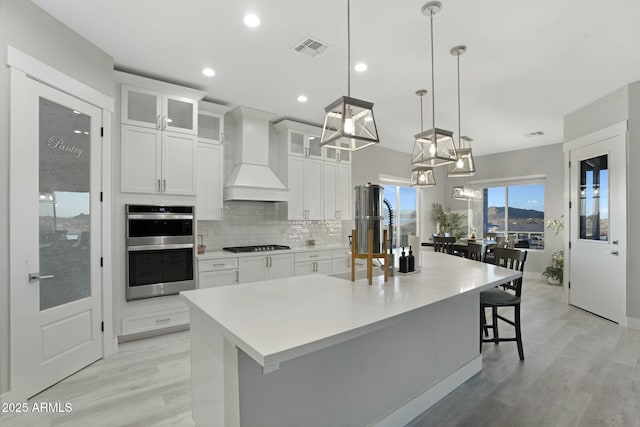 kitchen with black gas cooktop, stainless steel double oven, premium range hood, visible vents, and tasteful backsplash