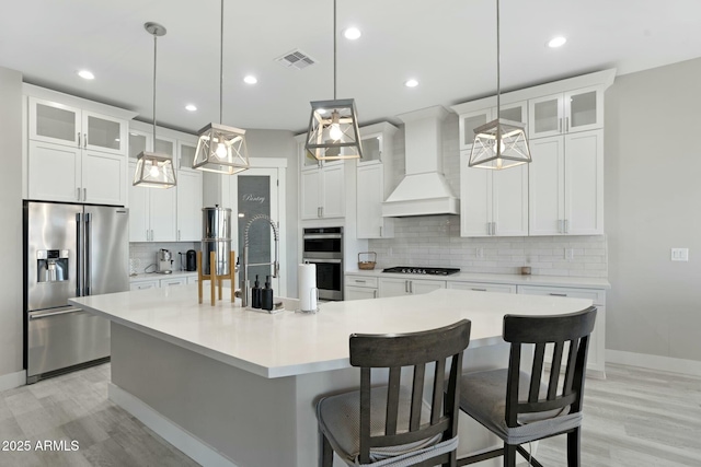 kitchen featuring white cabinets, decorative backsplash, a spacious island, custom exhaust hood, and stainless steel appliances