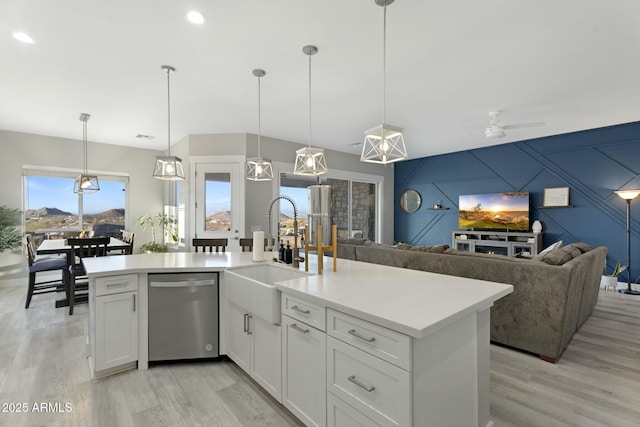 kitchen featuring an accent wall, a sink, open floor plan, light countertops, and dishwasher