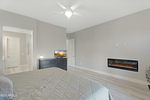 bedroom featuring ceiling fan, a glass covered fireplace, light wood-style flooring, and baseboards