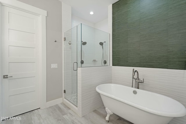 full bathroom featuring tile walls, a soaking tub, a shower stall, and baseboards