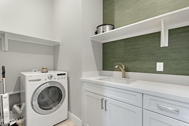 clothes washing area with washer / clothes dryer, cabinet space, a sink, and baseboards