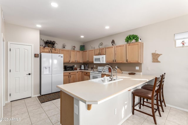 kitchen featuring sink, light brown cabinets, kitchen peninsula, white appliances, and a kitchen bar